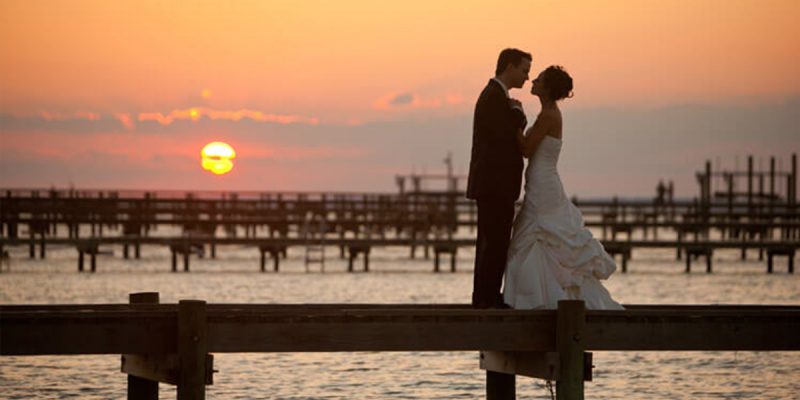 bride and groom standing on pier on the beach during sunset in emerald isle, nc
